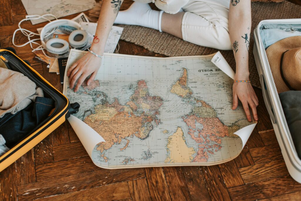 pexels photo 7368277 7368277 A traveler plans a journey, sitting on the floor with a world map and suitcase filled with essentials.