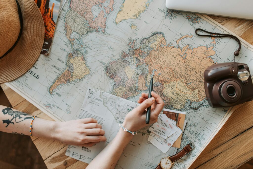 pexels photo 7368300 7368300 Top view of a woman's hands planning a trip with a map, camera, and travel items.