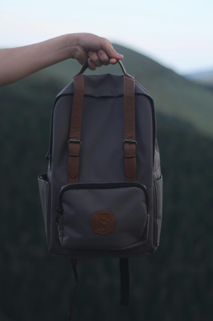 How to One Bag and Why You Should Consider it for Your next Trip A person holding a stylish gray backpack with leather straps, set against a natural outdoor background.